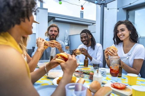 Cheerful multi ethnic friends savoring burgers and drinks while enjoying a lively rooftop barbecue
