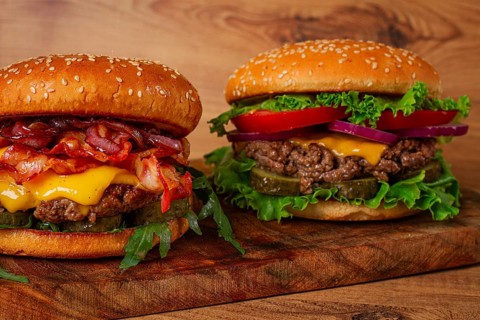 Two burgers with beef patty, fried bacon, cheddar cheese, tomatoes, homemade, no people