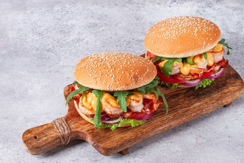 Two shrimp burgers and buns with sesame seeds, bacon, lettuce, tomatoes and onions, On a wooden
