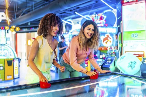 Two young women enjoying a friendly game of air hockey in a vibrant arcade, illuminated by colorful