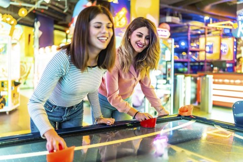 Two young women enjoying their free time playing air hockey in a colorful and modern amusement