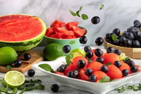 Grapes fall on fruit bowl with watermelon, lime and mint in front of ingredients