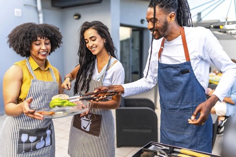 Happy multi ethnic friends preparing grilled vegetables and meat, enjoying barbecue party on the