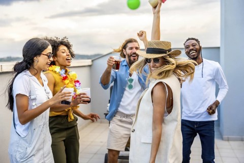 Cheerful multi ethnic friends enjoying cocktails while dancing joyfully at a vibrant rooftop party,