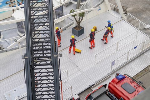Several firefighters stand on a platform next to a crane jib, fire brigade exercise for gondola