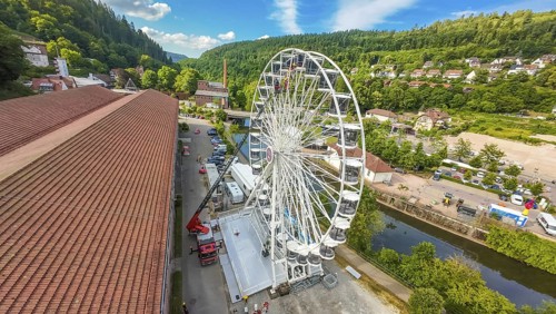 View of a Ferris wheel in a wooded environment with red roofs and blue sky, fire brigade exercise