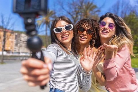 Three cheerful young women enjoying a summer day in the city, capturing a fun selfie with a gimbal,