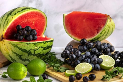 Sliced watermelon, grapes and limes on a wooden board with mint leaves