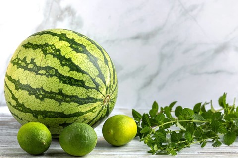 Watermelon and limes with mint leaves on a wooden surface
