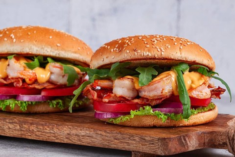 Two shrimp burgers and buns with sesame seeds, bacon, lettuce, tomatoes and onions, On a wooden
