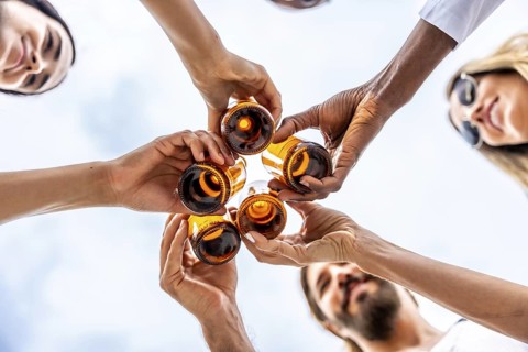 Group of diverse friends are holding and toasting glass bottles of beer together, celebrating under