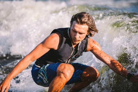 A man is surfing on a surfboard drawn by a motor boat above the wave of the boat. Weixerfer is