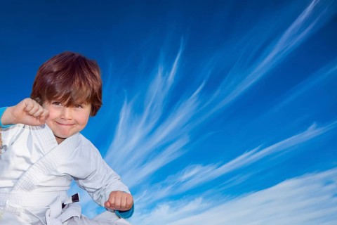 Handsome boy in a white kimono practices judo. Background - flying cirrus clouds and blue sky.
