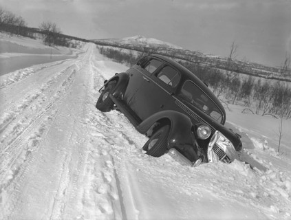 Winter driving in the 1930s. A car has skidded of the snowy road down and is stuck in the snow