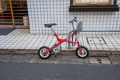 Small red folding bike with basket attached to railing