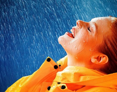 A woman joyfully embracing the rain in a yellow raincoat, expressing freedom and happiness