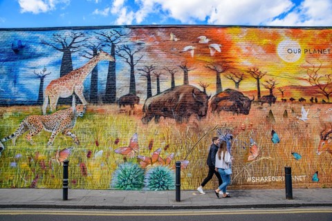 People passing by the graffiti wall art at Brick Lane Market in London, United Kingdom
