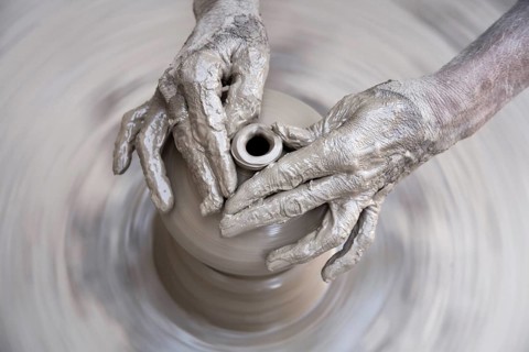 Pottery, artist muddy hands making clay pot giving shape on spinning wheel, semi urban village