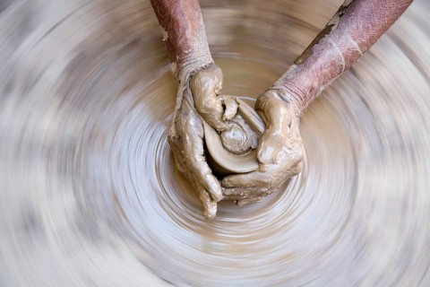 Pottery, artist muddy hands making clay pot giving shape on spinning wheel, semi urban village