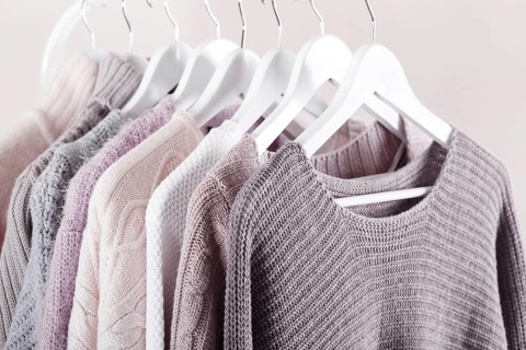 Warm knitted, autumn, winter clothes hanging on a rack, trending concept, pastel colours