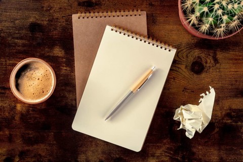 Notebook with a pen, coffee, and plant, overhead flat lay shot on a rustic wooden desk, with a