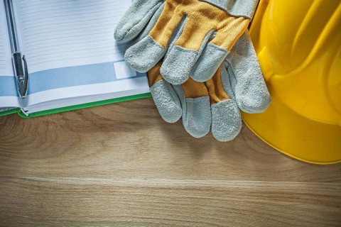 Protective gloves notepad pen safety hard hat on wooden board
