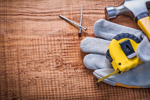Tapeline glove hammer nails on vintage wooden board with copyspace construction concept