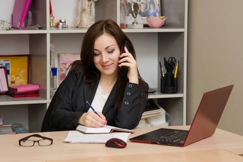 Business woman writing in a notebook and talking on phone