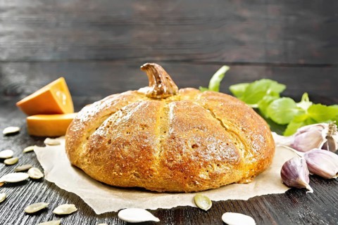 Pumpkin bread on paper, garlic, basil, pieces and seeds of a vegetable on the background of a dark