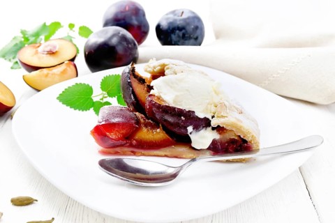 Piece of sweet pie with plum, sugar, cardamom and ice cream in a plate, sprigs of green mint, towel