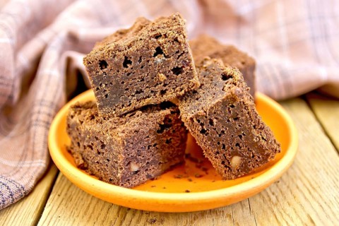 Piece of chocolate cake in a clay plate, napkin on a wooden boards background