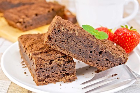 Two pieces of chocolate cake on a plate with strawberries and mint on a fork against a linen