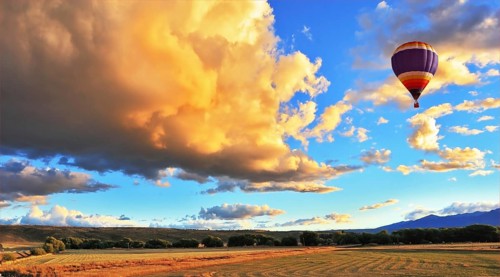 The huge rain cloud lit orange sunset. In the sky flying multicolored balloon