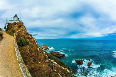 The white building of the lighthouse looks spectacular on a high cape. New Zealand. Nugget Point