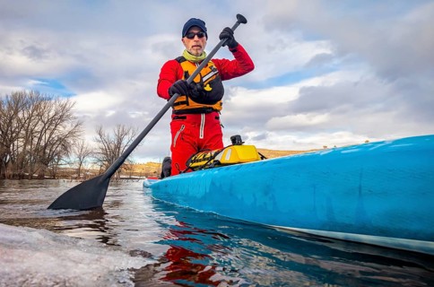 Senior paddler in a dry suit and life jacket is training on stand up paddleboard on a mountain lake