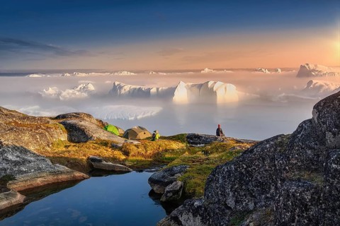Large glaciers in the bay by the rocky shore in the light of the setting sun with fog over the