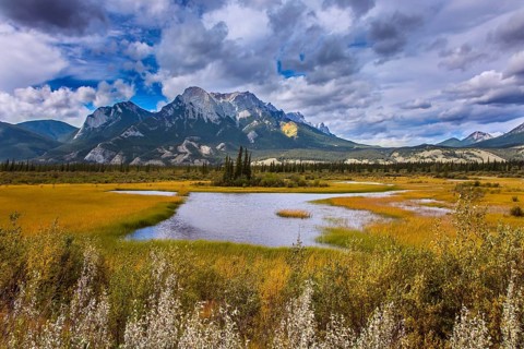 Cloudy Indian summer in the Rockies of Canada. Rocks, lakes and yellow grass under flying clouds.