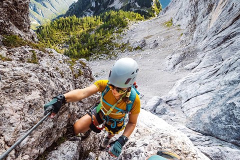 Caucasian woman mountaineer climbing up the mountain on via ferrata trail, high up in the mountain
