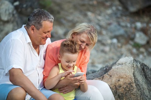 Happy grandparents and grandson with smartphone outdoor. Grandmother and grandfather watching the