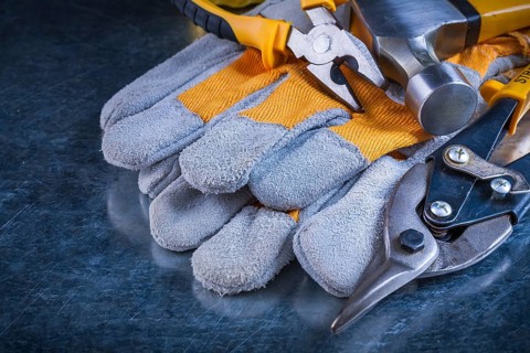 Protective gloves with claw hammer pliers and tin snips on scratched vintage metallic background