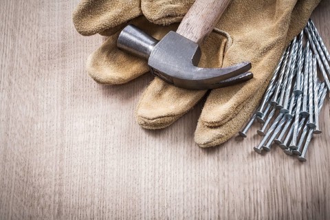 Claw hammer leather protective gloves and heap of metal nails on wooden board close up version