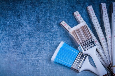 Wooden meter paintbrushes on scratched metallic background construction concept