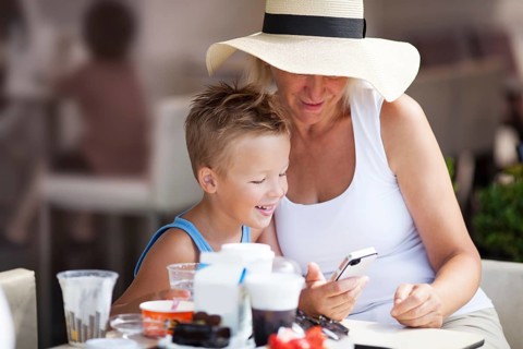 Smiling Mature Woman and Young Boy On Vacation Using Cell Phone Together on Outdoor Restaurant