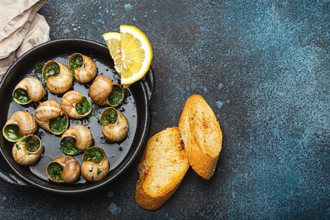 Escargots de Bourgogne Snails with Garlic Butter and Parsley in black cast iron pan with Lemon and