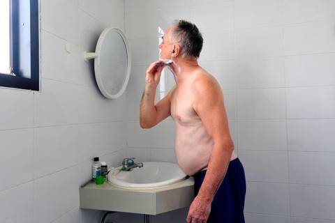 Man 60 plus shaves wet in the bathroom