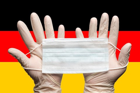 Doctor holding medical face mask in two hands in white gloves on background flag of Germany.
