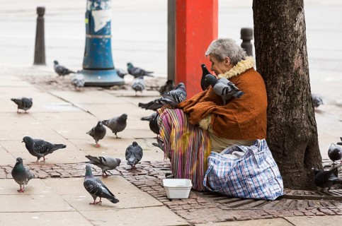 Sofia, Bulgaria - February 27, 2016: A homeless beggar woman is covered by pigeons while begging at