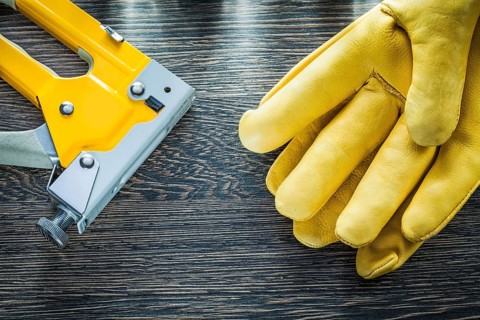 Pair of protective gloves construction stapler on wooden board