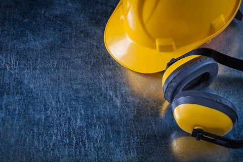 Noise insulation ear muffs and hard hat on scratched metallic background copy space image
