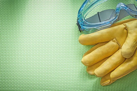 Safety glasses leather gloves on green background construction concept